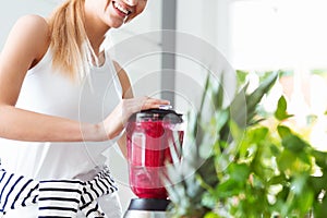 Smiling woman blending red smoothie photo