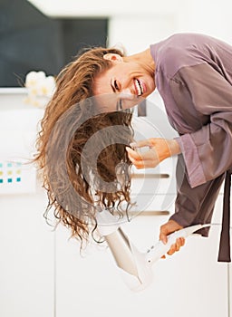 Smiling woman blow drying hair in bathroom