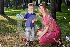 Smiling woman and boy play with bubbles outdoors.