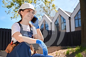 Smiling woman builder in uniform talking phone during break at work