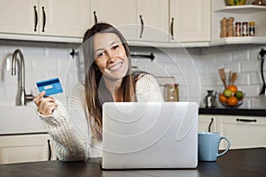 Smiling woman buying online with credit card and laptop at home