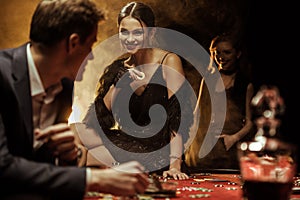 Smiling woman with casino chip sitting on poker table and looking at man