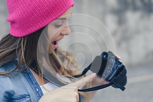 Smiling woman in casual clothes and pink hat holding camera and showing good shot she made during the street photo shooting. Close