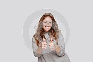 Smiling woman in casual wear showing thumb up against white studio wall background