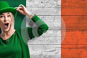 Smiling woman celebrates St. Patrick\'s Day. Beautiful woman in a green hat. Irish flag as background