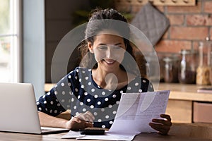 Smiling woman checking financial documents, calculating bills, using laptop