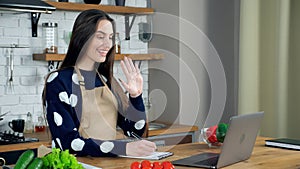 Smiling woman chef teacher in apron greets housewife student teaches online
