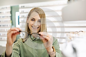 Smiling woman choosing new optical glasses to buy in optics store