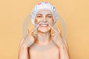 Smiling woman with clean skin and patches under her eyes doing skin care procedure pointing at her white perfect teeth dental oral