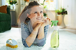 Smiling woman with cleaning agent and brush laying on carpet