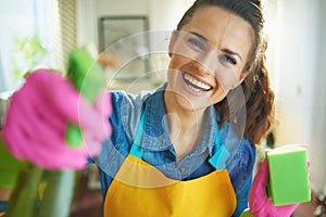 Smiling woman with cleaning agent and sponge housecleaning