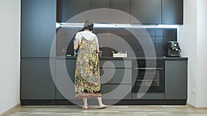 Smiling woman cleaning modern kitchen, dancing and listening to music in headphones. Happy female in casual home wear having fun a