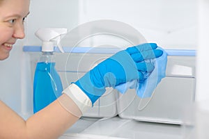 Smiling woman cleans the refrigerator with a rag and soapy liquid.