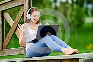 Smiling woman in cordless headphones works using laptop outside.