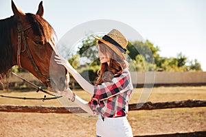 Smiling woman cowgirl taking care of her horse on farm