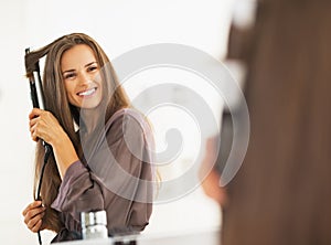 Smiling woman curling hair with straightener