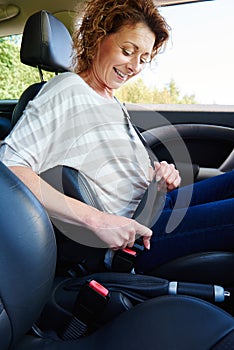 Smiling woman with curly hair buckling seat belt in car