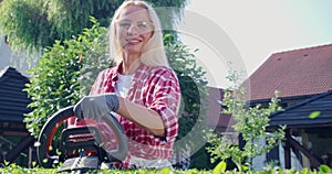 Smiling woman cutting bushes with electric trimmer