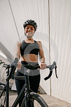 Smiling woman cyclist in protective gear standing with her bike while training outdoors
