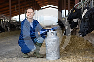 Smiling woman dairy farm worker posing with milk can in cowshed