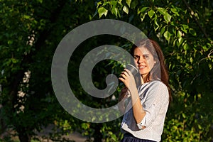 Smiling woman with dark hair holding black paper coffee cup in a garden looks at the camera