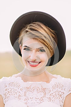 The smiling woman with the deep green eyes, red lipstick, cateyes and black hat is looking at the camera. The close-up