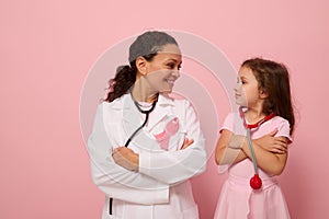 Smiling woman doctor and cute baby girl looking at each other, wearing pink ribbon, symbol of Breast Cancer Awareness Day,