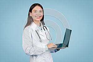 Smiling woman doctor using laptop on light blue background