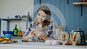 Smiling woman doing online shopping using smartphone and credit card while have breakfast in the kitchen at home