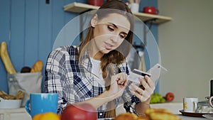 Smiling woman doing online shopping using smartphone and credit card while have breakfast in the kitchen at home