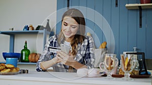 Smiling woman doing online shopping using smartphone and credit card while have breakfast in the kitchen at home