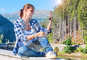 Smiling woman is doing selfie osit on the walls in the mountain
