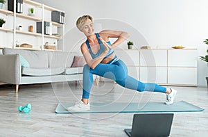 Smiling woman doing twist lunges on mat using pc