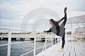 Smiling woman doing yoga exercise outdoors on the beach pier