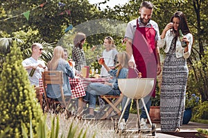 Smiling woman drinking beer while her friend grilling food during birthday outdoor party