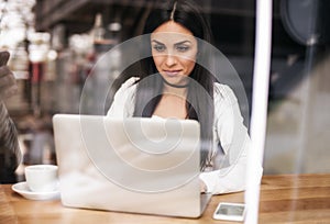 Smiling woman drinking coffee and surfing on internet. Cafe wind