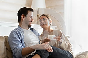 Smiling woman drinking hot beverage, sitting on loving husband laps