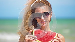 Smiling woman eating watermelon on beach. Woman eating tasty summer fruit. Happy summer time.