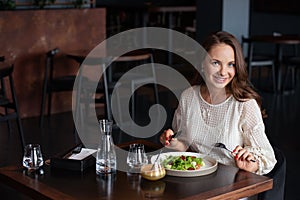 Smiling woman eats vegetarian salad in cafe