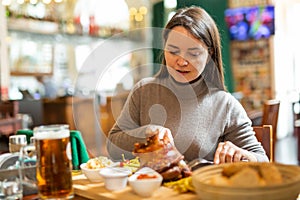 Smiling woman enjoying baked pork knuckle in restaurant