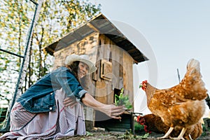 Smiling woman enjoying farm life while feeding her chickens