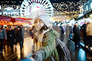 Smiling woman at everning festive Christmas fair holding someone hand, follow me. ferris wheel on background.