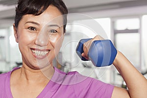 Smiling woman exercising with weights, arm raised, in the gym