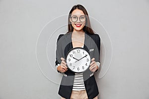 Smiling woman in eyeglasses holding clock and looking at camera