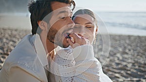 Smiling woman feeding husband sitting beach sand sunny evening close up.