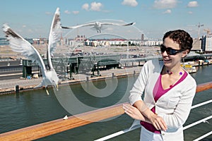 Smiling woman feeds seagulls on deck of ship