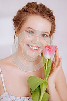 Smiling woman feels joy and happiness, holds a pink tulip.