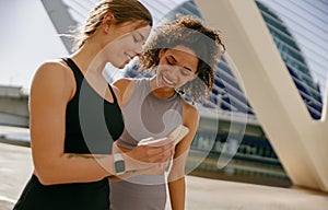 Smiling woman with female friend looking on smartphone before exercising standing outdoors