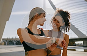 Smiling woman with female friend looking on smartwatch before exercising standing outdoors