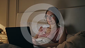 Smiling woman finishing work in night bed. Happy girl resting closing computer